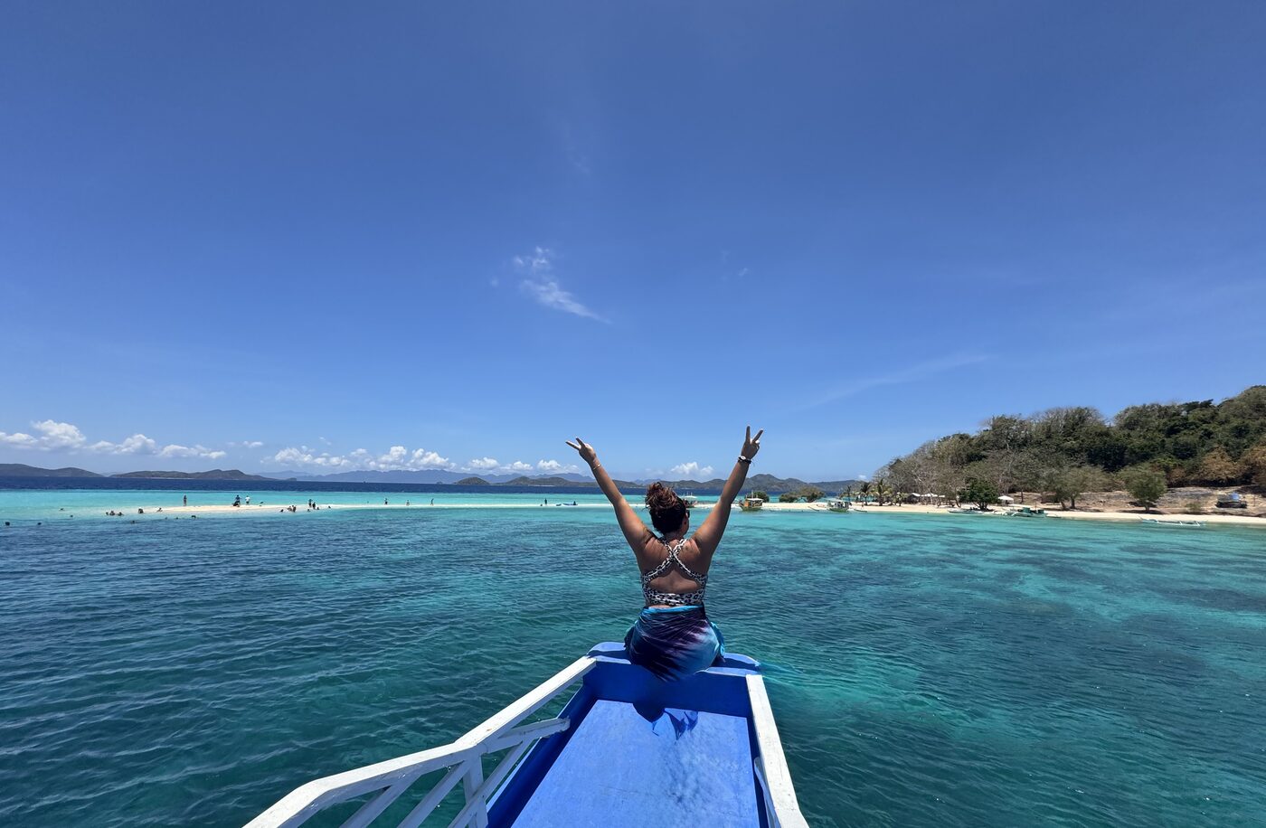Karlee with her arms up on the bow of a boat over turquoise water