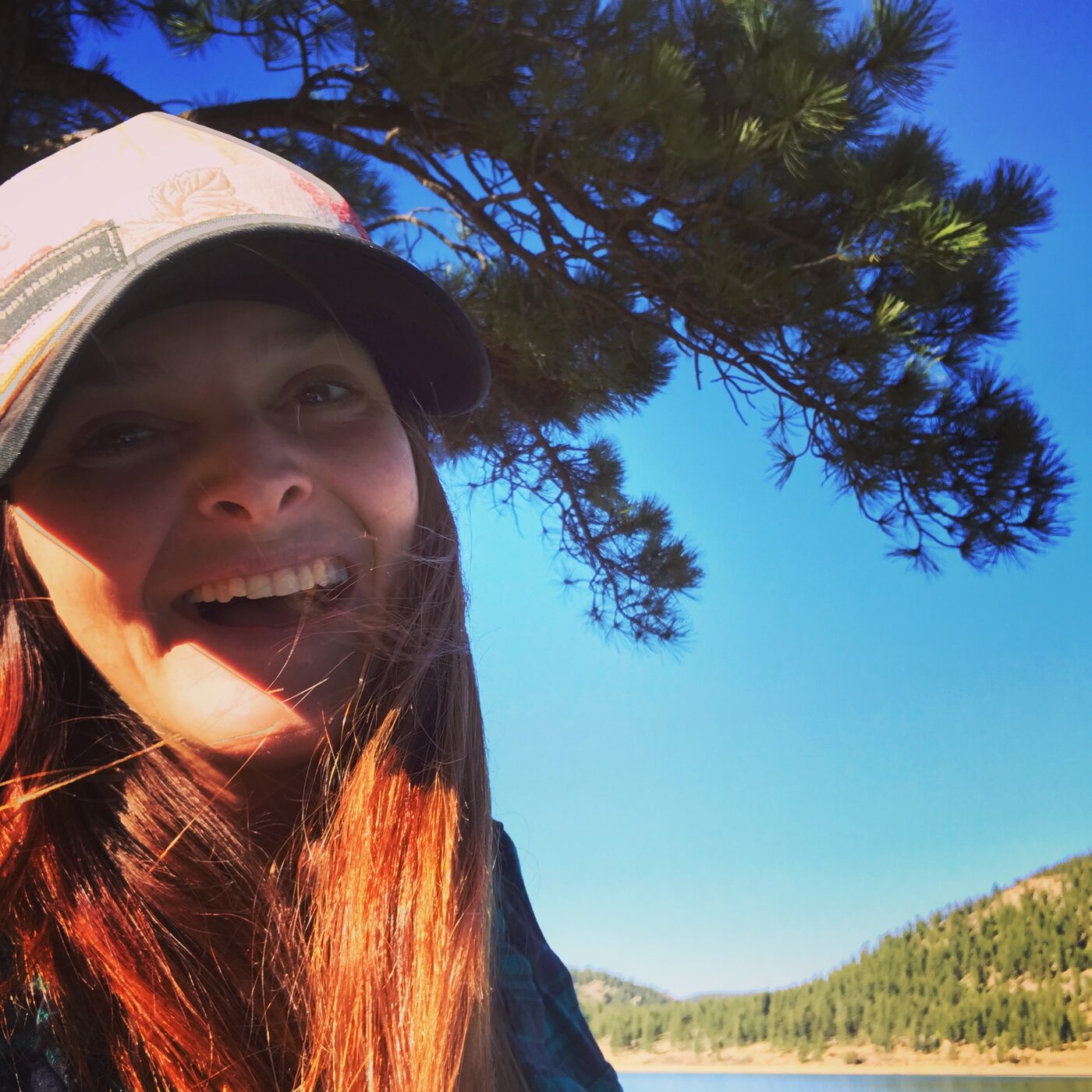 Karlee laughing under a pine tree by a lake