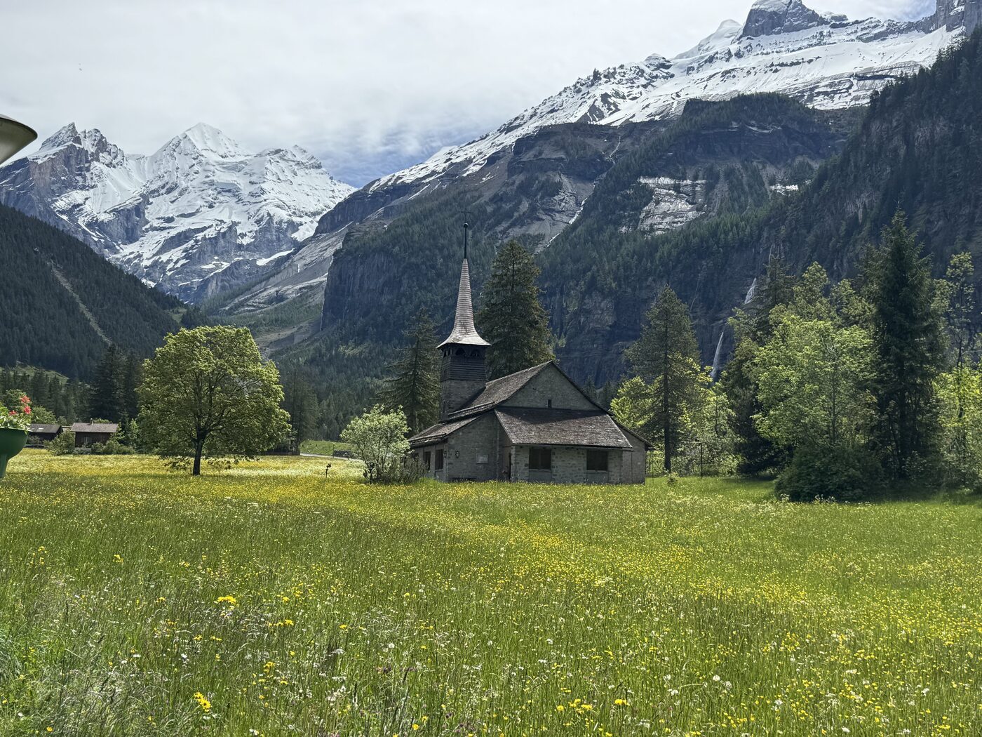 A small stone chapel in a meadow of wildflowers below snowy peaks in Kandersteg