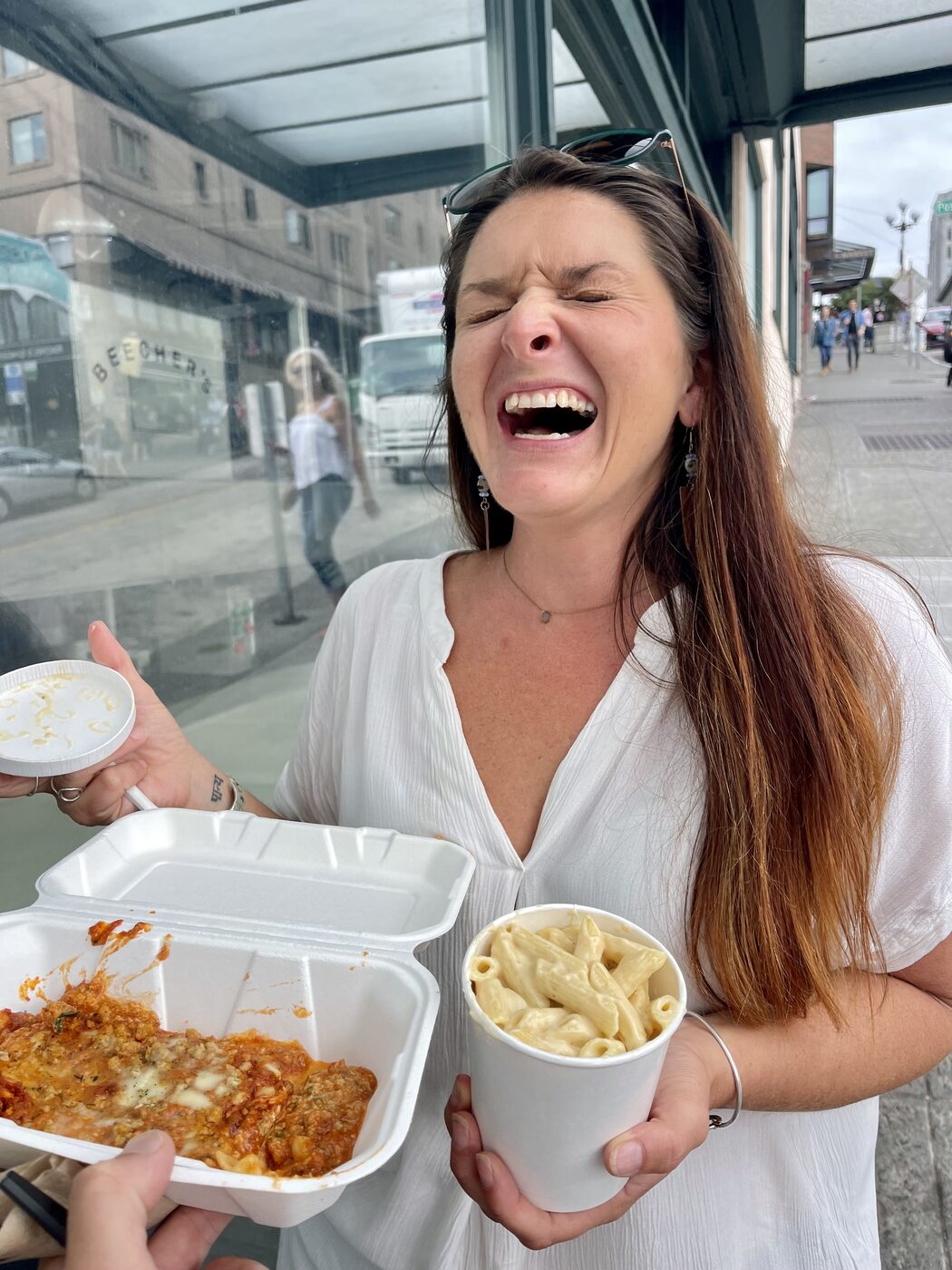 Karlee laughing outside Beecher's in Seattle, holding a cup of mac and cheese and a box of pasta