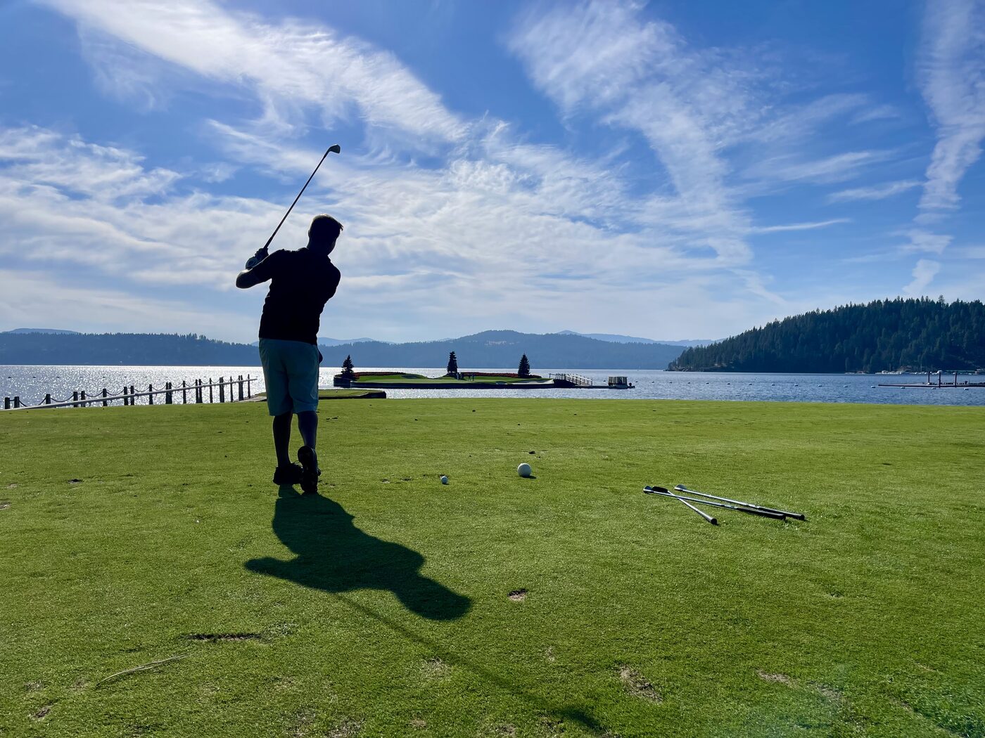 Jesse mid swing on a lakeside tee in Coeur d'Alene, with the floating green out on the water