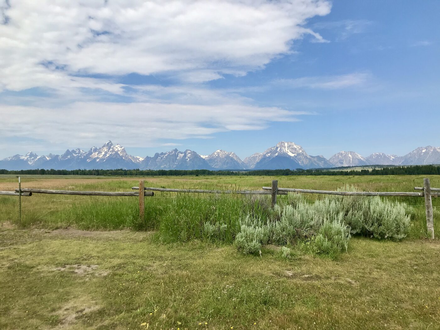 The Teton range across a sagebrush meadow and a wooden fence