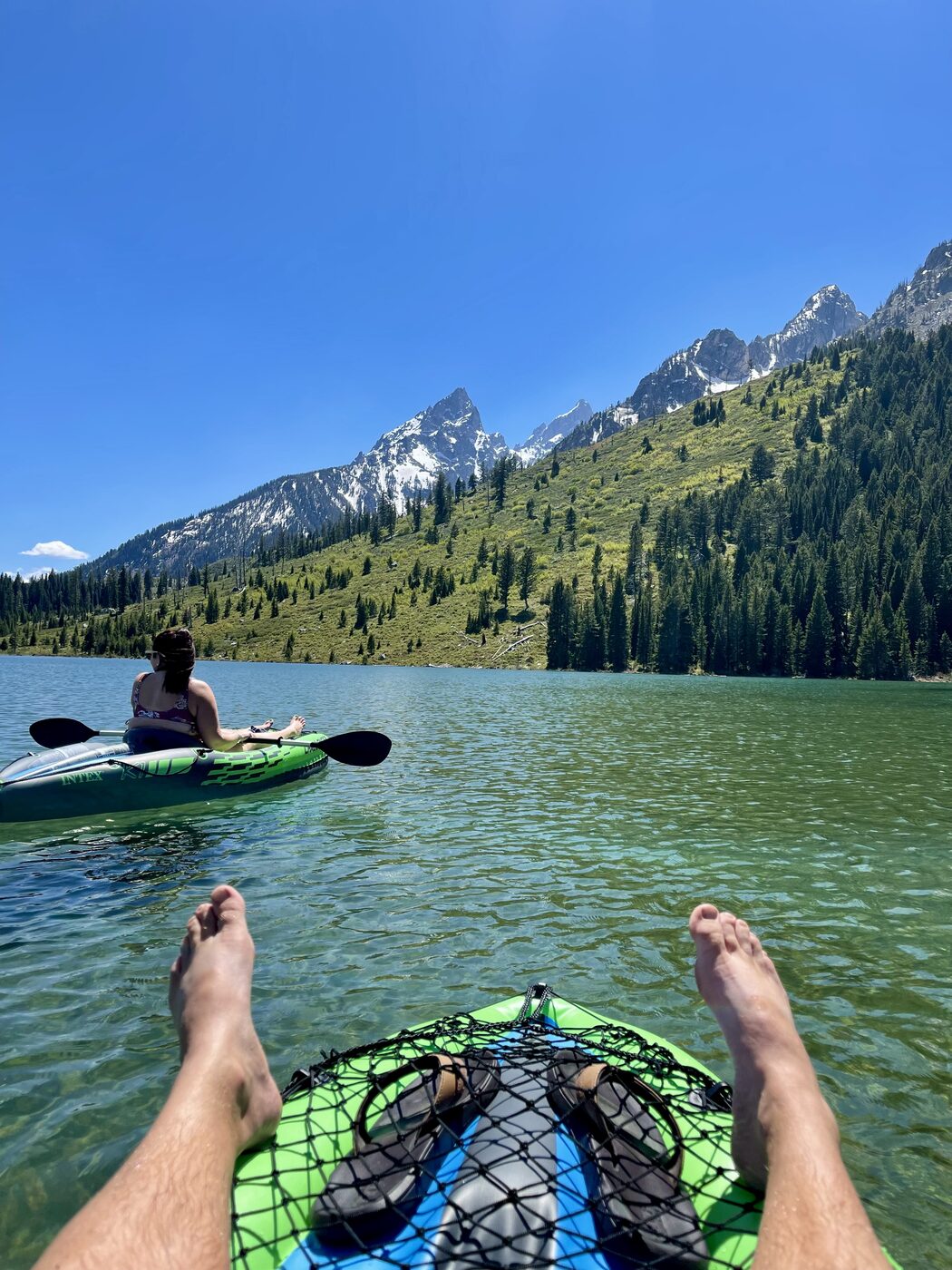 View from an inflatable kayak with the Tetons above the water and a second kayak ahead