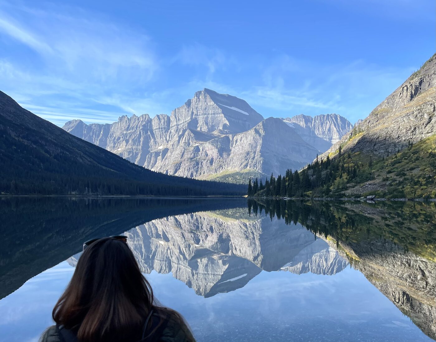 Mountains reflected in a still lake in Glacier National Park, one of us looking out across the water