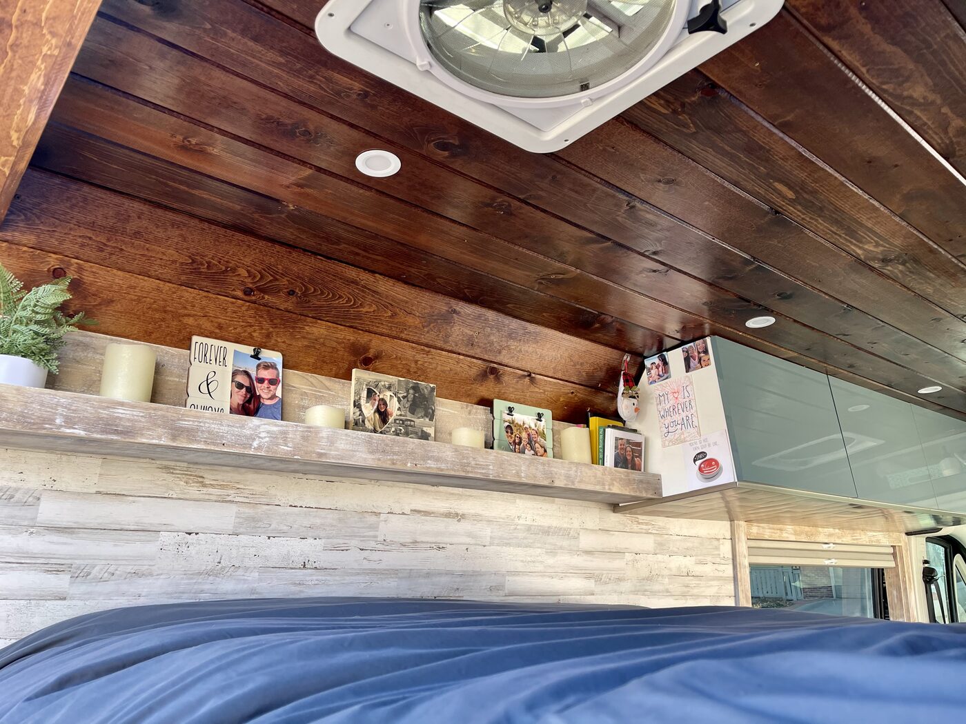 The bed under the wood ceiling, with photos lined up on the shelf above it